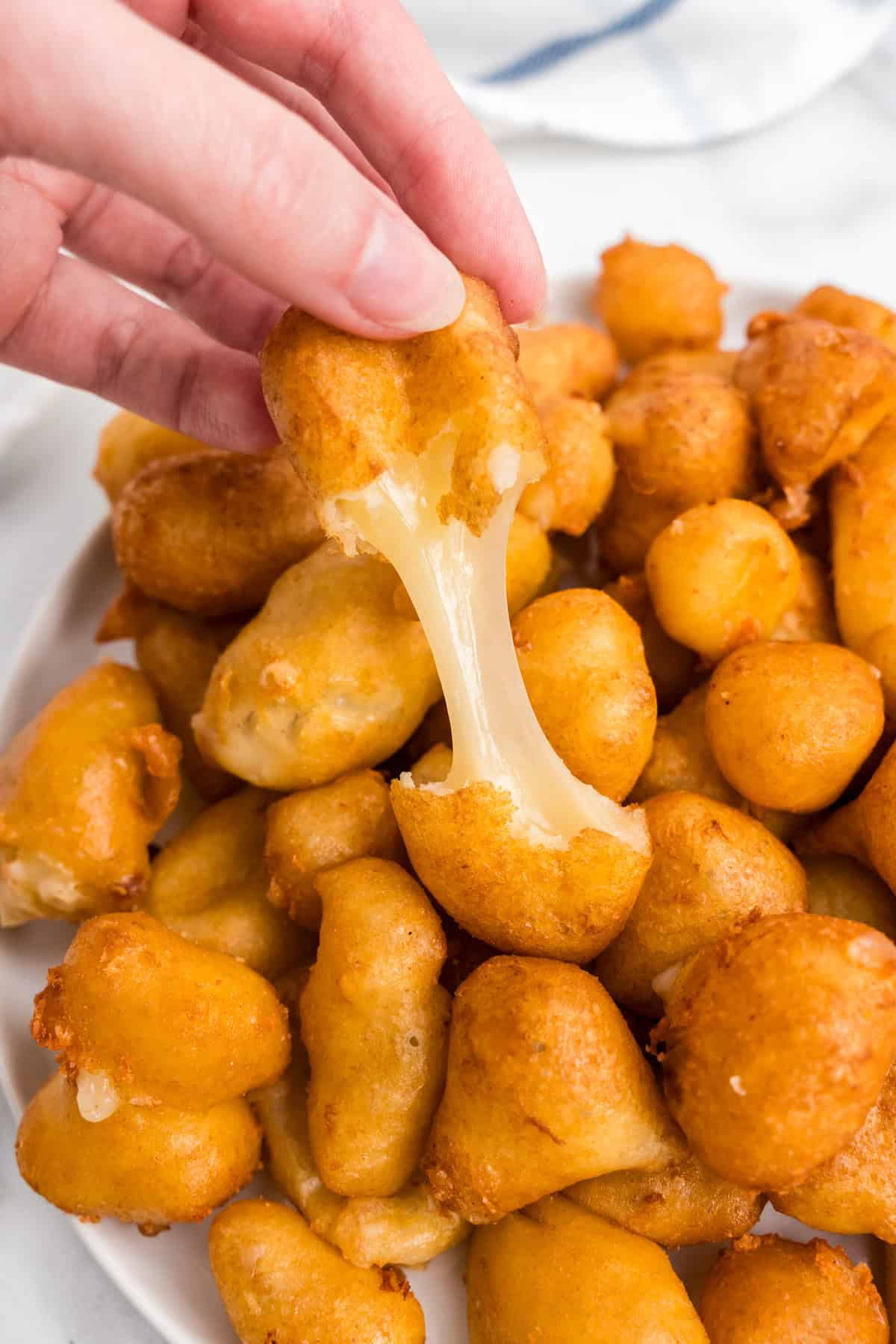 Cheese Curds piled in serving dish, using fingers to pull apart one of the curds