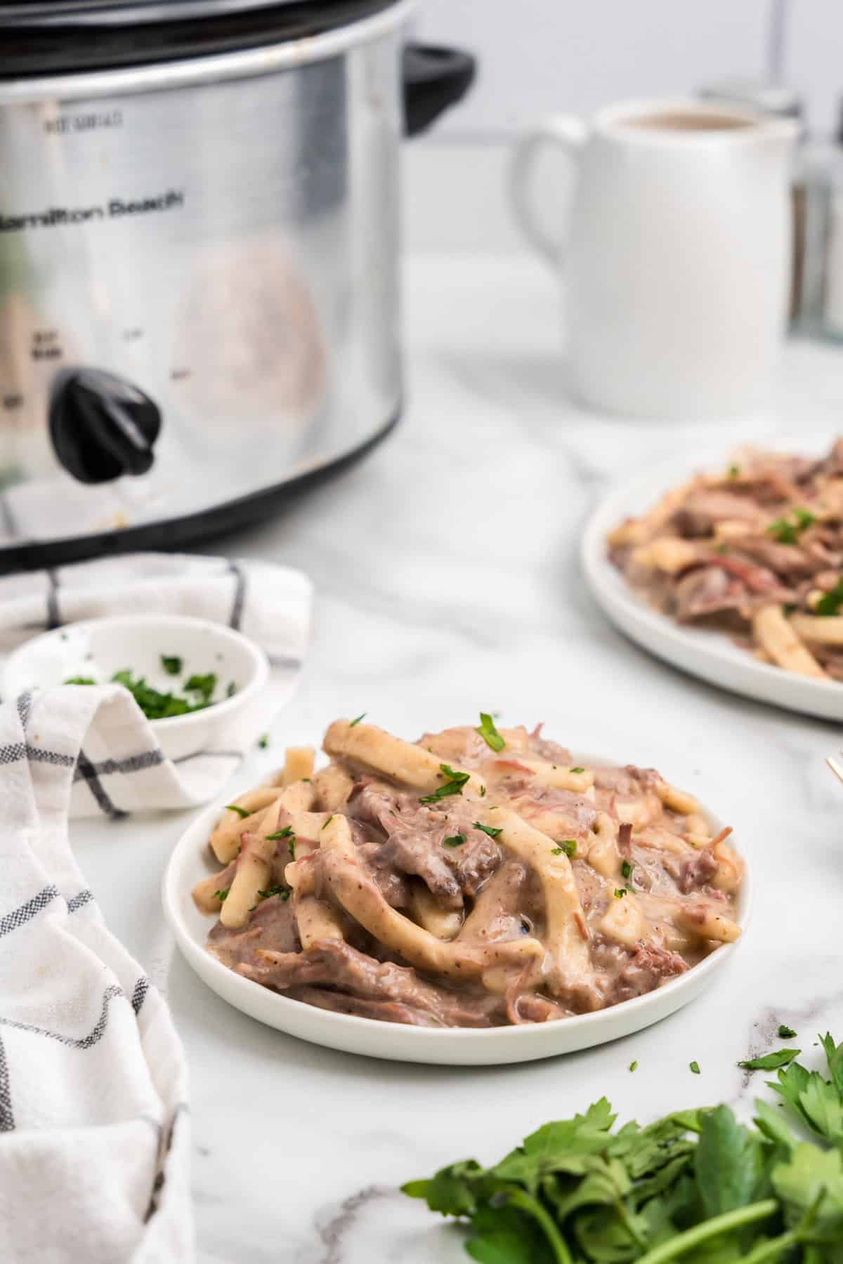 Crock Pot Beef and Noodles in shallow serving bowl with crock pot in background