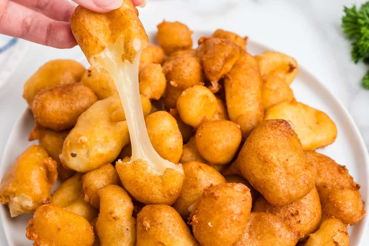 Cheese Curds piled in serving dish, using fingers to pull apart one of the curds
