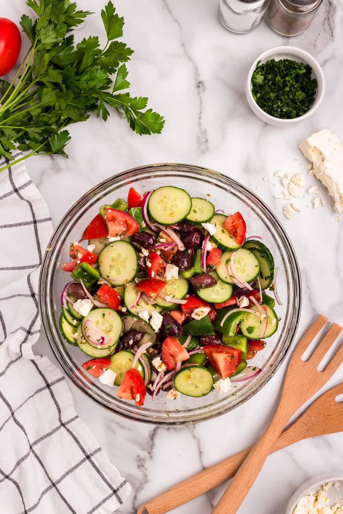 Tossed ingredients for Greek Salad in glass serving bowl