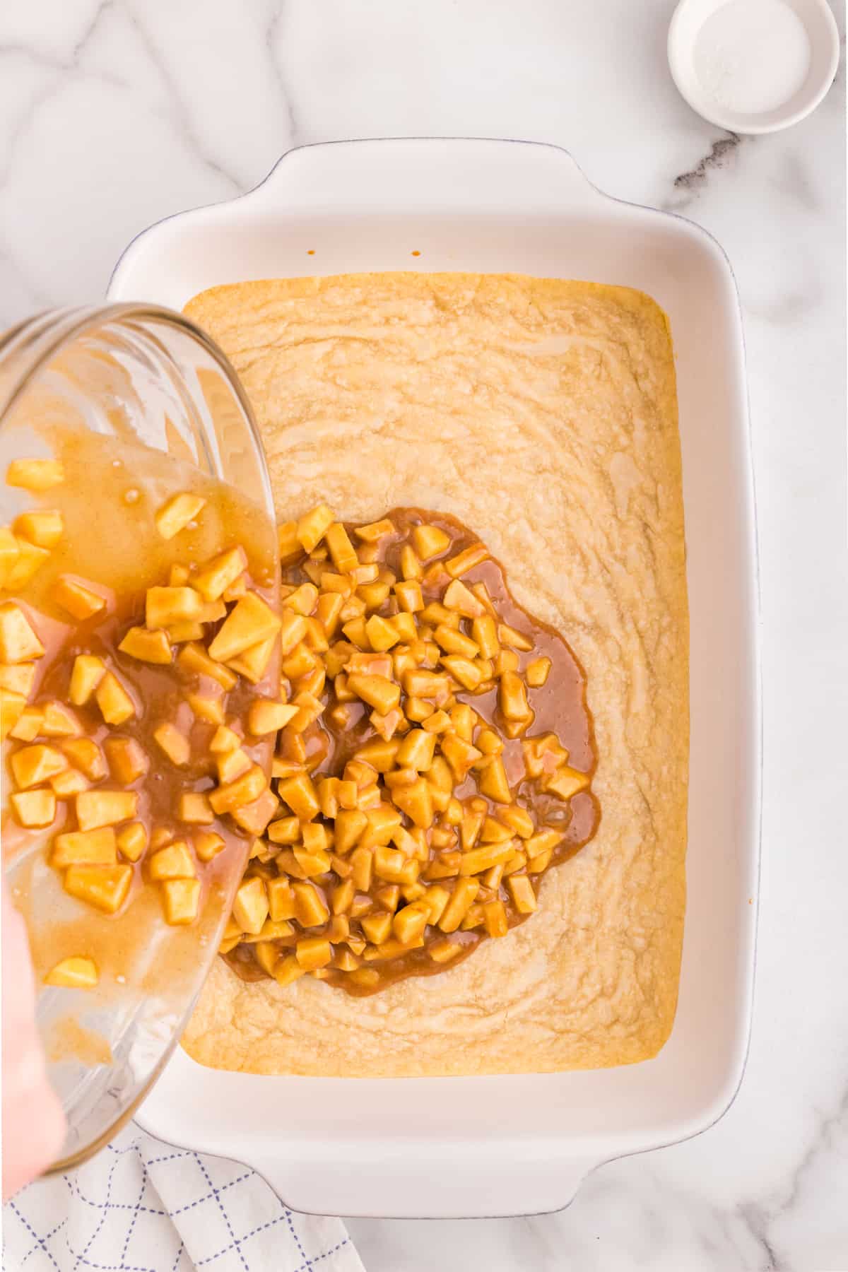 Pouring apple and caramel mixture over crust in 9x13 baking dish for Salted Caramel Apple Bars