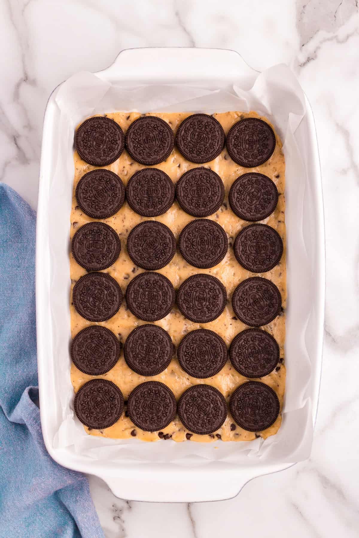 Closely lining Oreo cookies overtop of cookie base for Slutty Cheesecake Bars in 9x13 baking pan