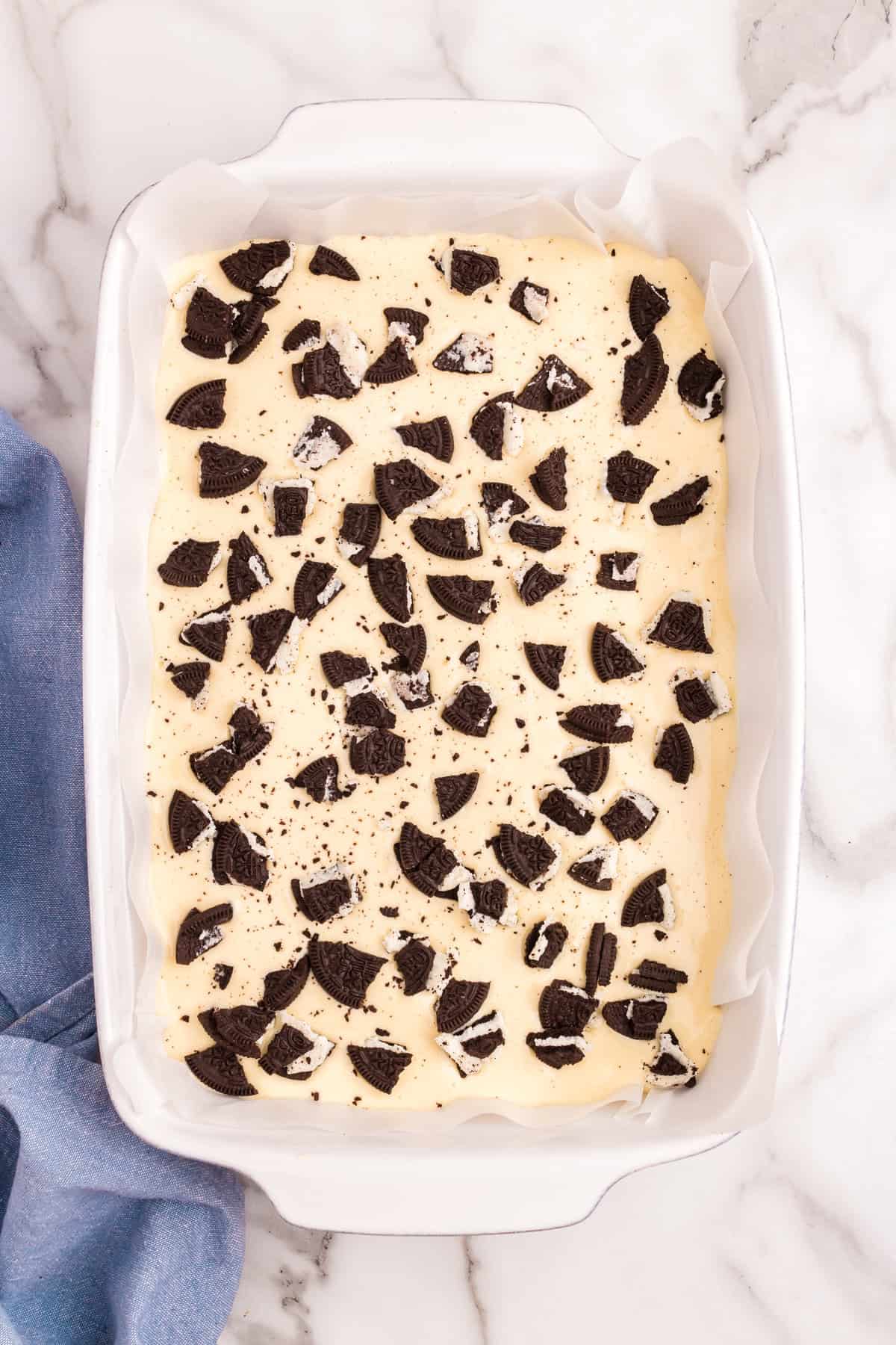 Adding Oreo pieces over cheesecake layer of Slutty Cheesecake Bars
