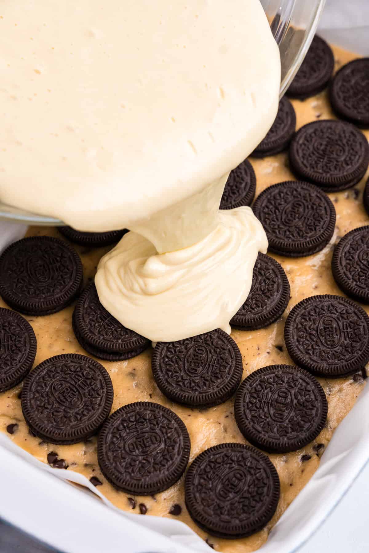 Pouring cheesecake batter over Oreo layer of Slutty Cheesecake Bars recipe 