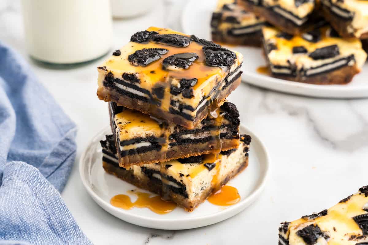 Slutty Cheesecake Bars stacked on a plate dripping with caramel