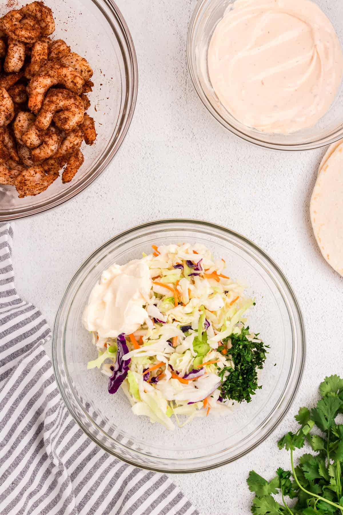 Coleslaw mixture adding to dressing in glass mixing bowl for Baja Shrimp Tacos