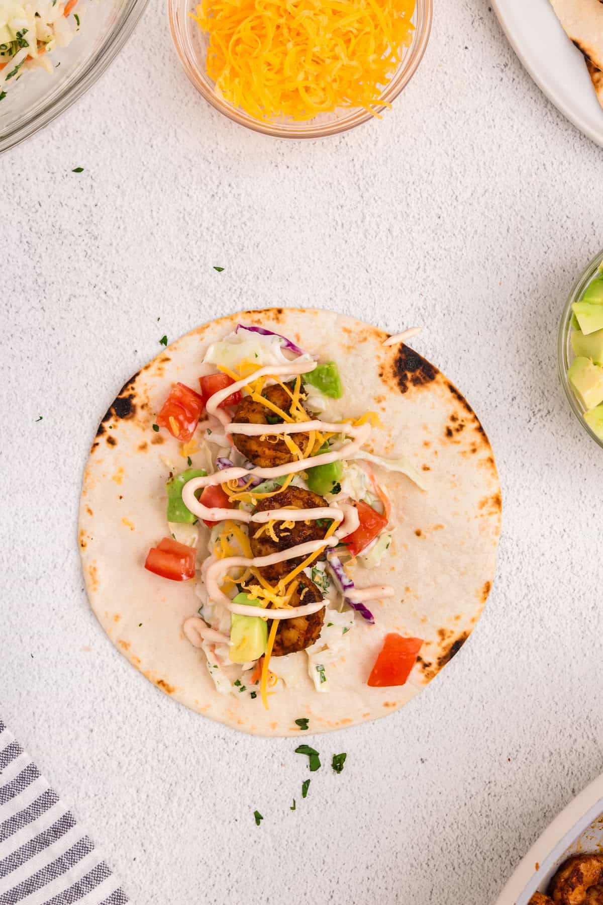 Piling Baja Shrimp Tacos ingredients and toppings in flour tortilla