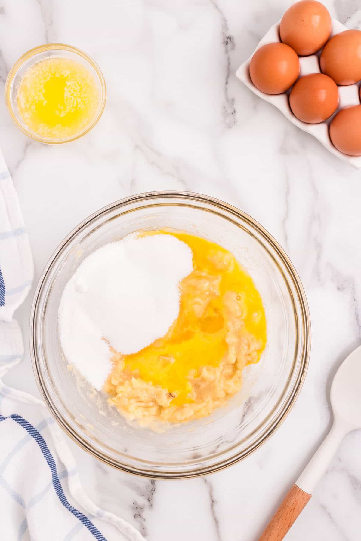 Wet ingredients and sugar in glass mixing bowl for Banana Crumb Muffins