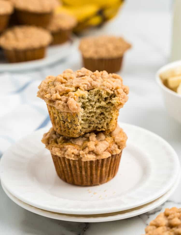 Banana Crumb Muffins stacked on white plate with one bite taken of the top muffin