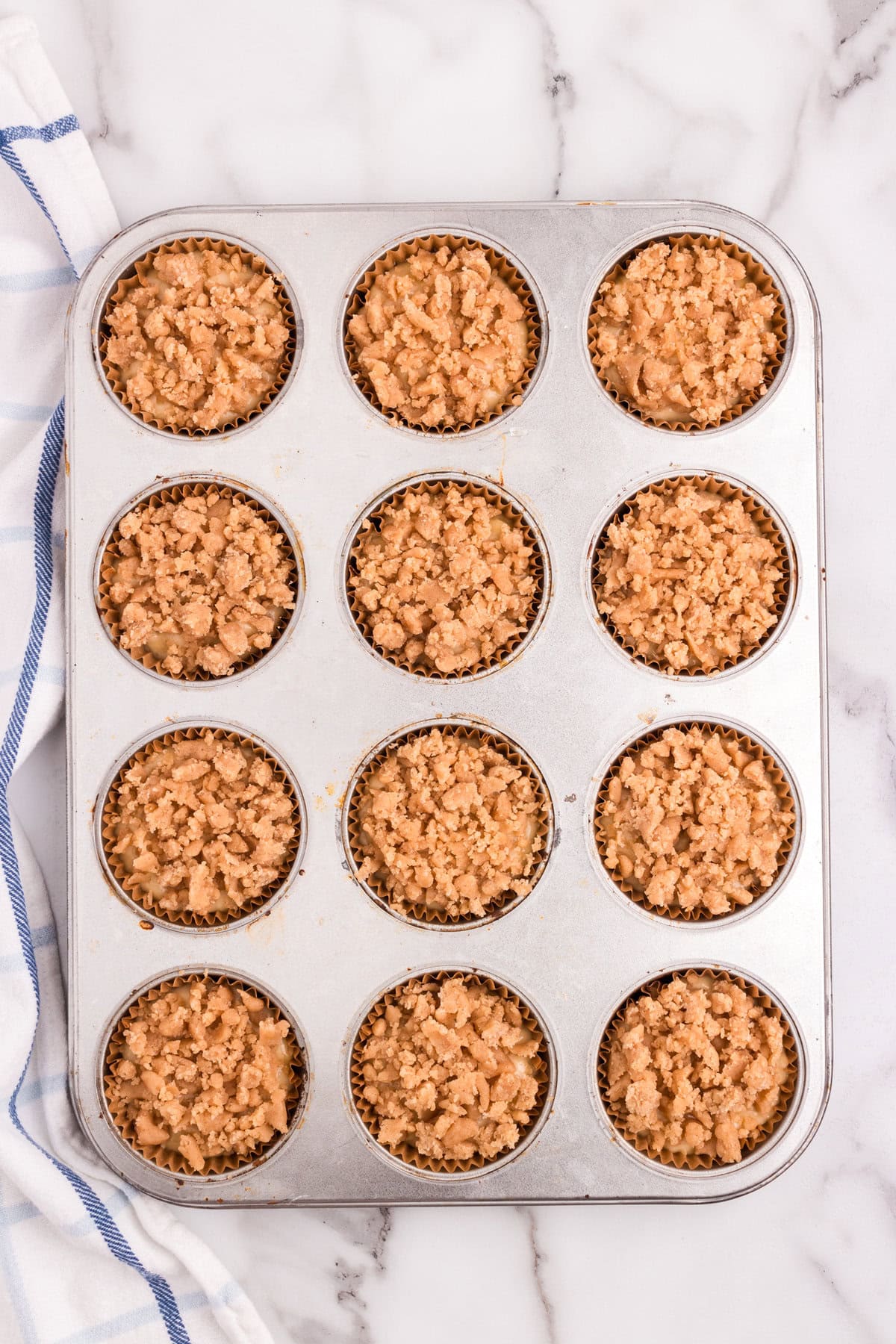 Adding crumb mixture overtop muffin batter in paper lined tins