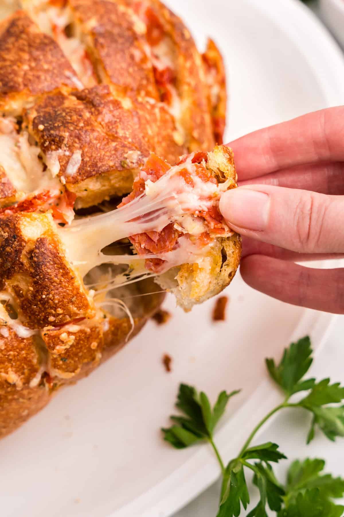 Using fingers to pull a 
 piece of Pull Apart Pizza Bread from loaf