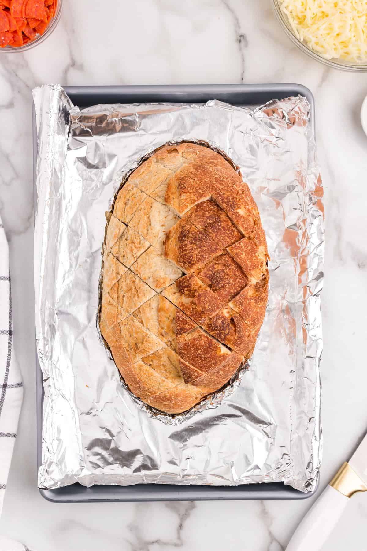 Italian bread loaf cut into criss-cross slices on tinfoil lined pan for Pull Apart Pizza Bread recipe