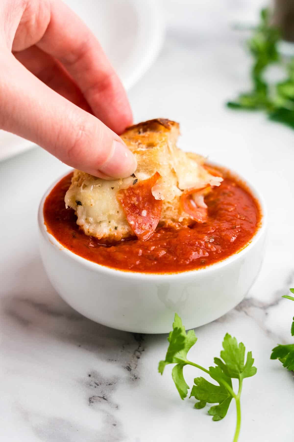 Dipping Pull Apart Pizza Bread piece in small bowl of marinara sauce