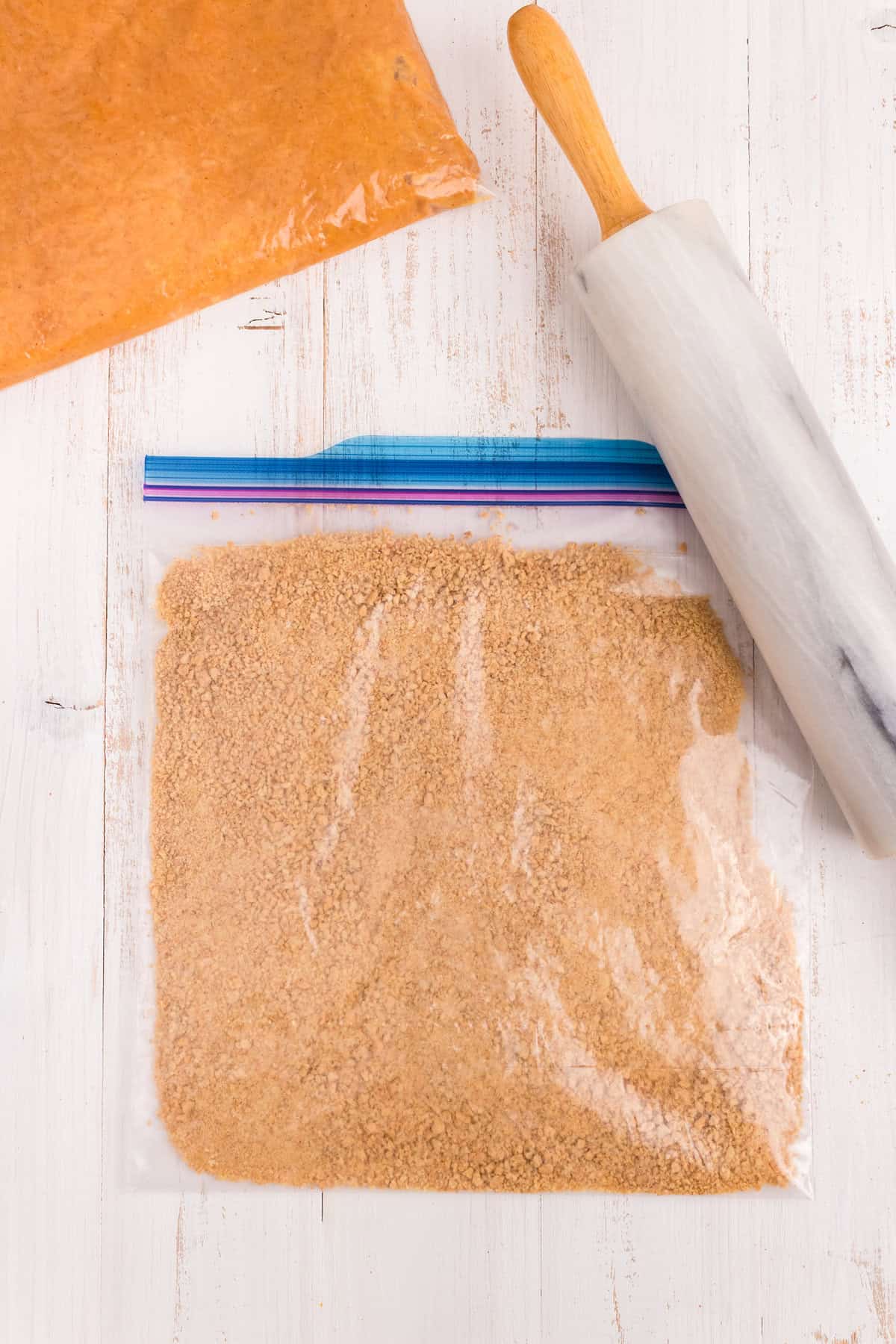 Crushing graham crackers for crust base with rolling pin in large zip lock bag