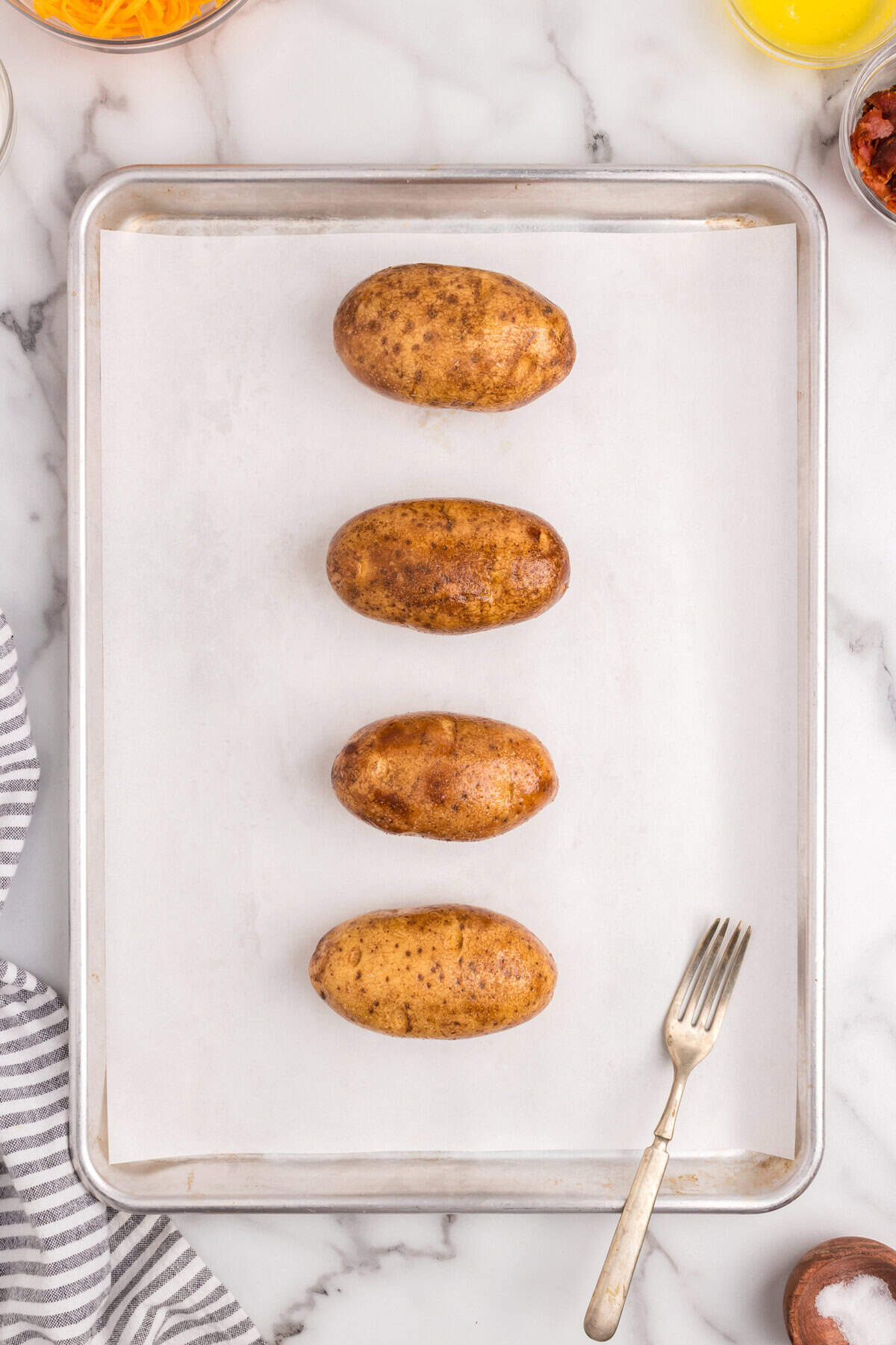 Russet potatoes on parchment-lined baking sheet prior to baking the first time after being pierced with fork