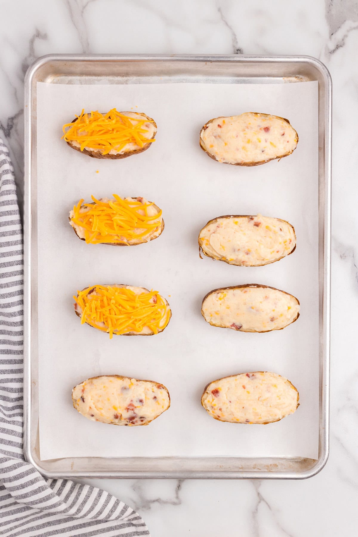 Spooning in the combined Twice Baked Potatoes ingredients into potato skins and topping with shredded cheese
