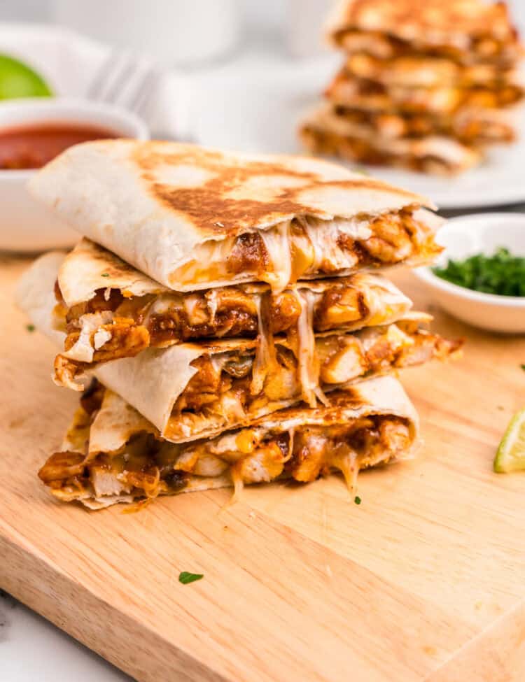 Chicken Quesadillas cut and stacked on wooden cutting board oozing with cheese