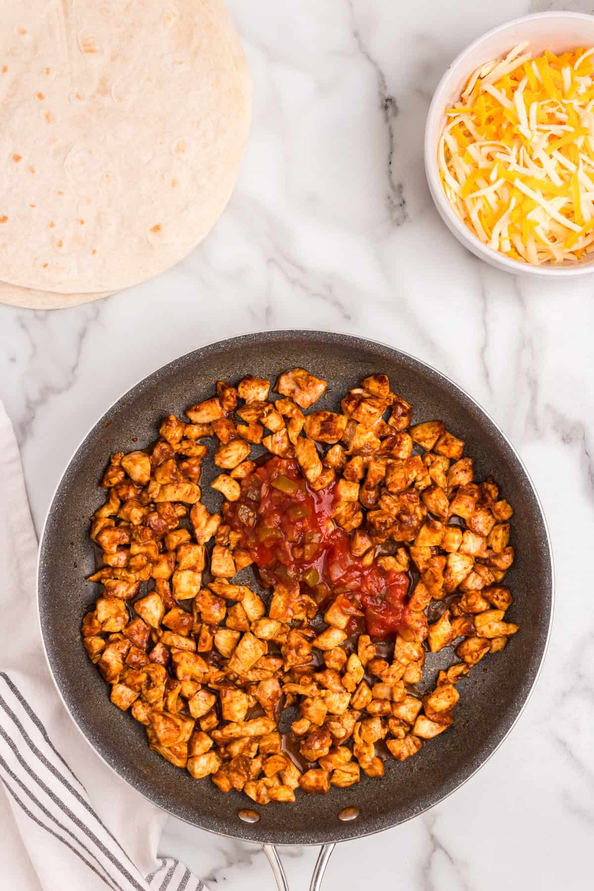Cooking seasoned chicken in stovetop skillet with olive oil and salsa for Cubed chicken coated in taco seasoning in small mixing bowl for Chicken Quesadilla recipe