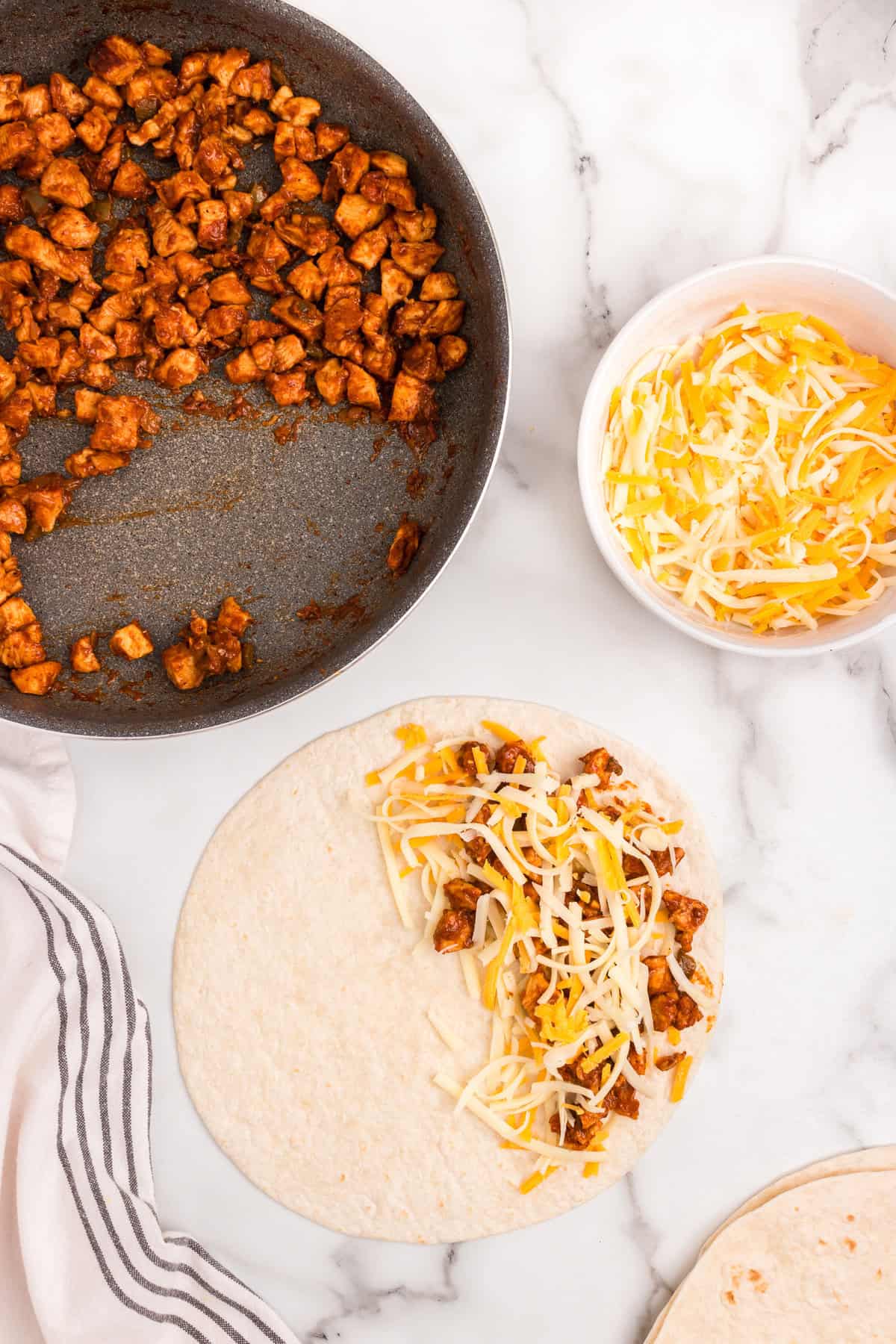Adding cooked chicken and shredded cheese to half of a burrito sized flour tortilla for Chicken Quesadillas