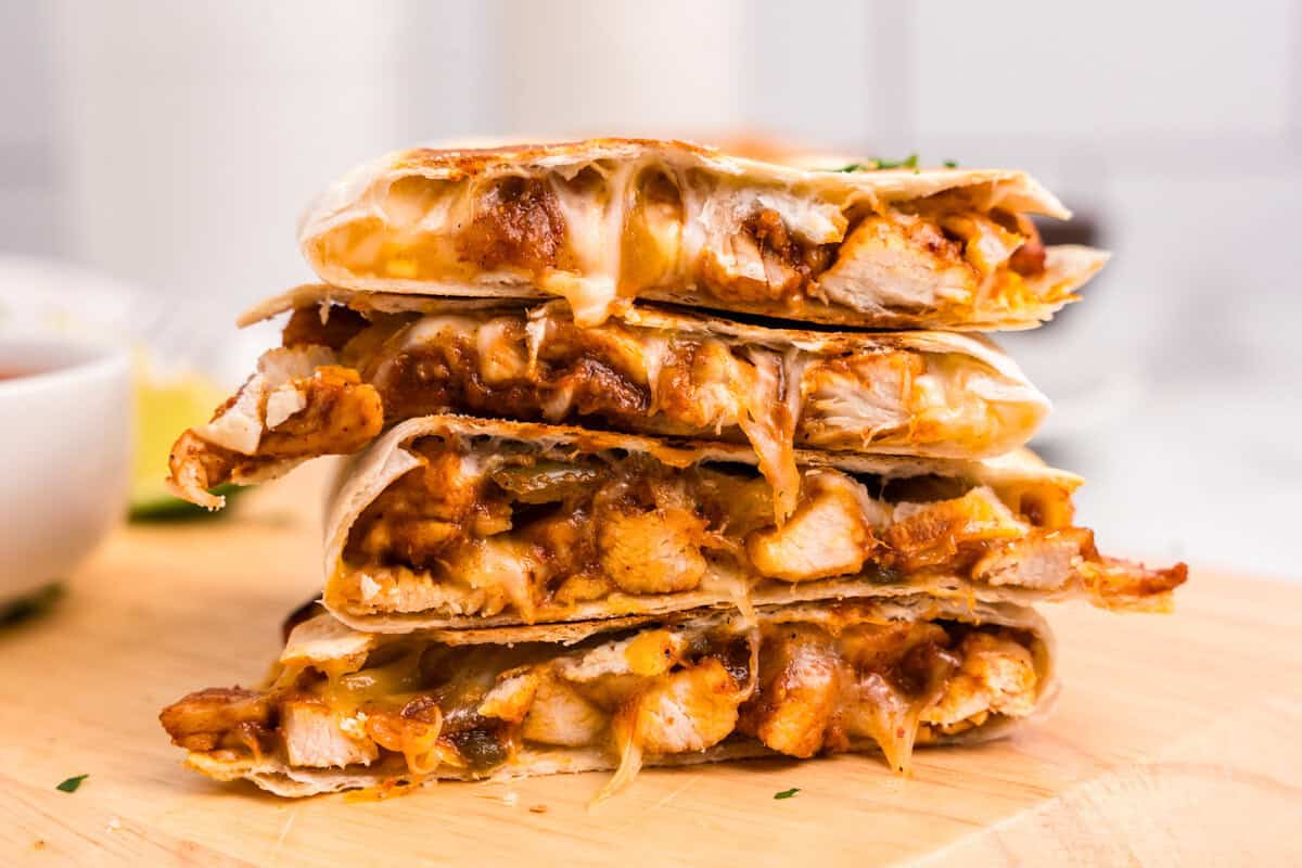 Chicken Quesadillas cut and stacked on wooden cutting board oozing with cheese