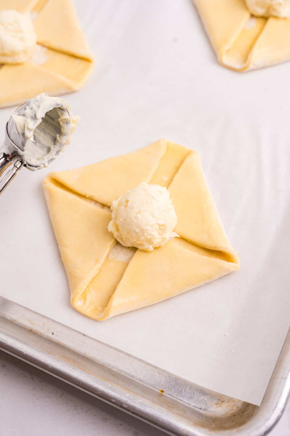 Folding the four corners of puff pastry into each other while scooping in cream cheese mixture into the center for Cream Cheese Danish recipe