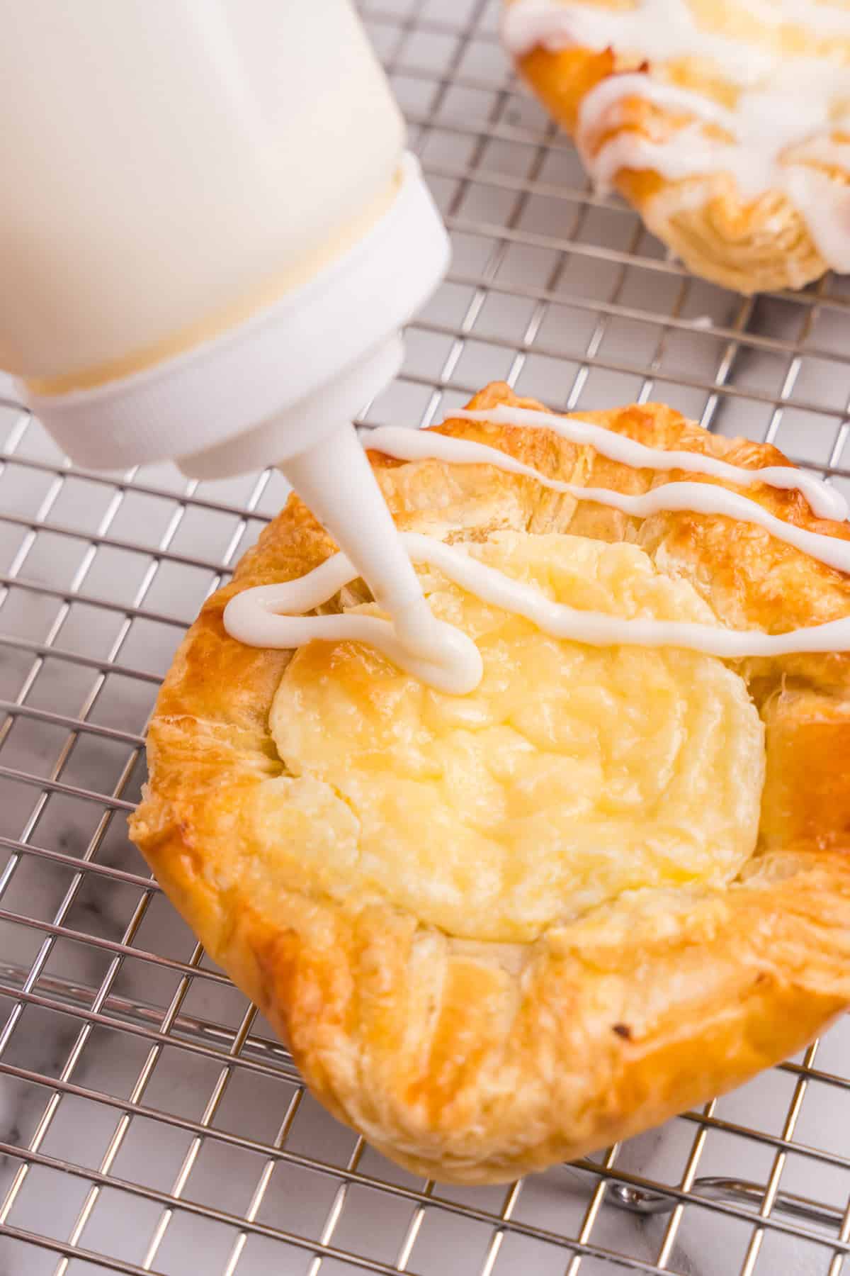 Squeezing lemon glaze onto Cream Cheese Danish on wire rack