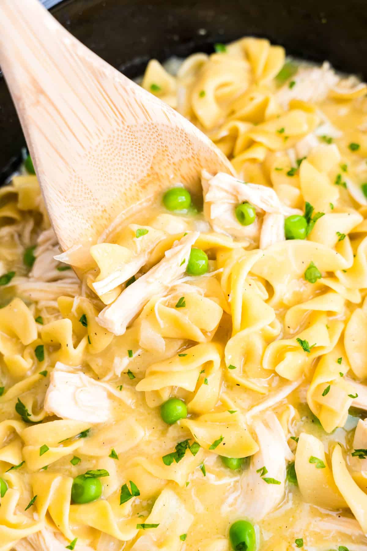 Wooden spoon scooping crockpot chicken and noodles out of crockpot