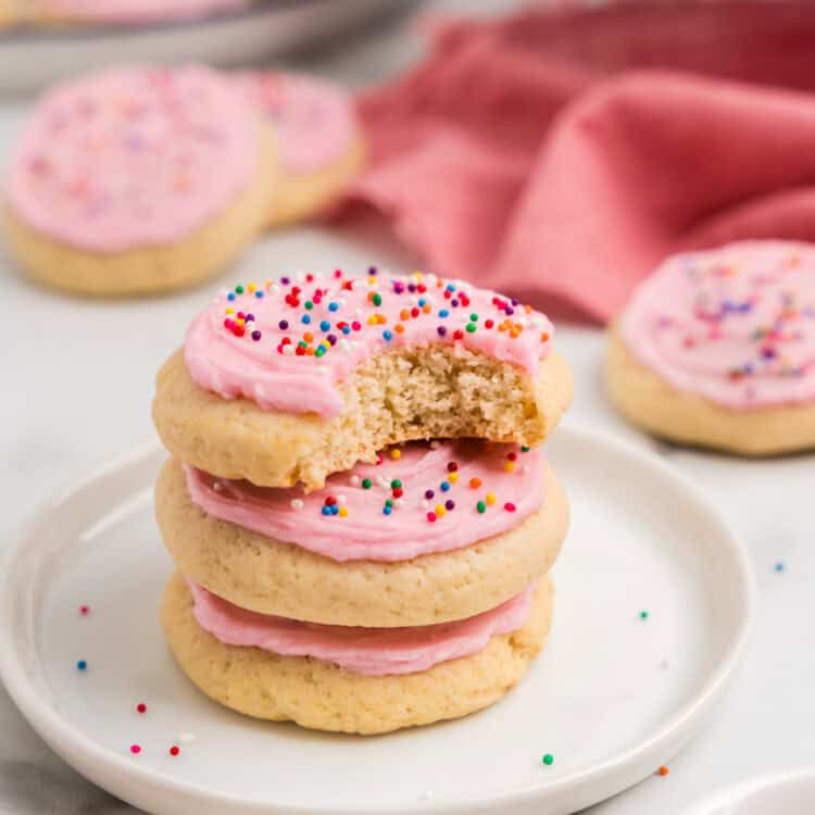 Sour Cream Cookies with homemade frosting and sprinkles stacked on plate with one bite taken