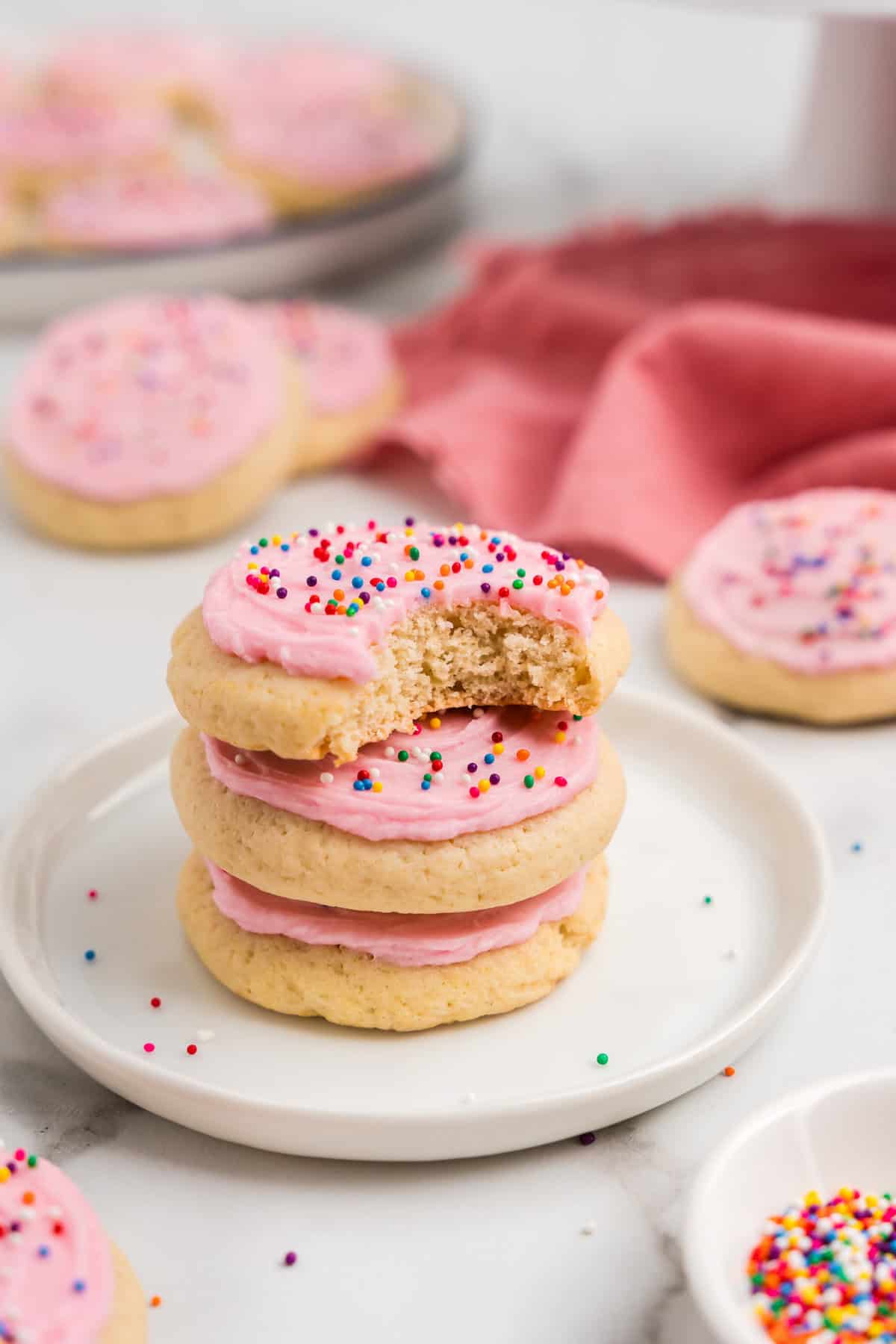 Sour Cream Cookies with homemade frosting and sprinkles stacked on plate with one bite taken