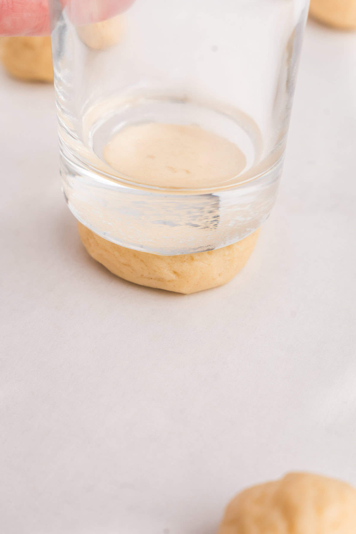 Pressing Sour Cream Cookie dough balls flat with glass before baking on cookie sheet