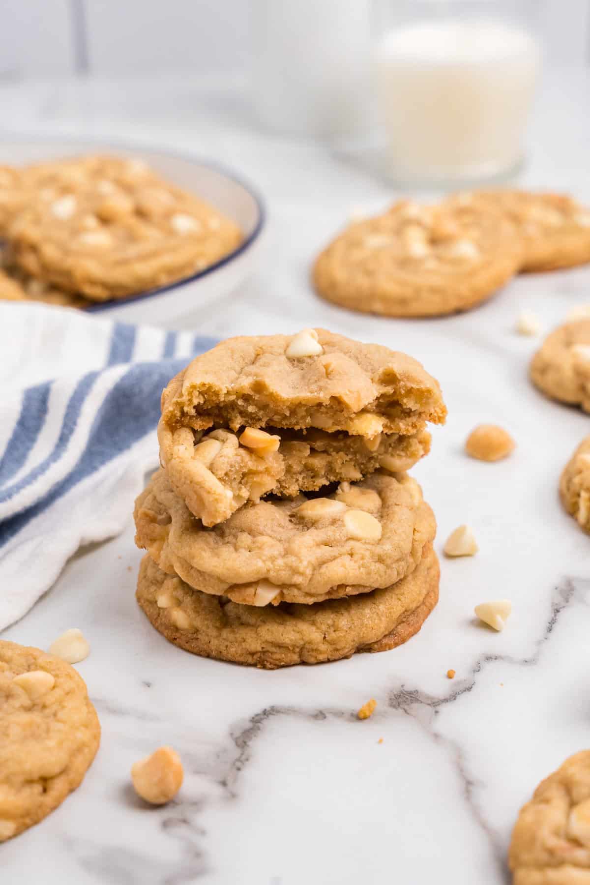 White Chocolate Macadamia Nut Cookies stacked with one bite taken with a glass of cold milk in the background