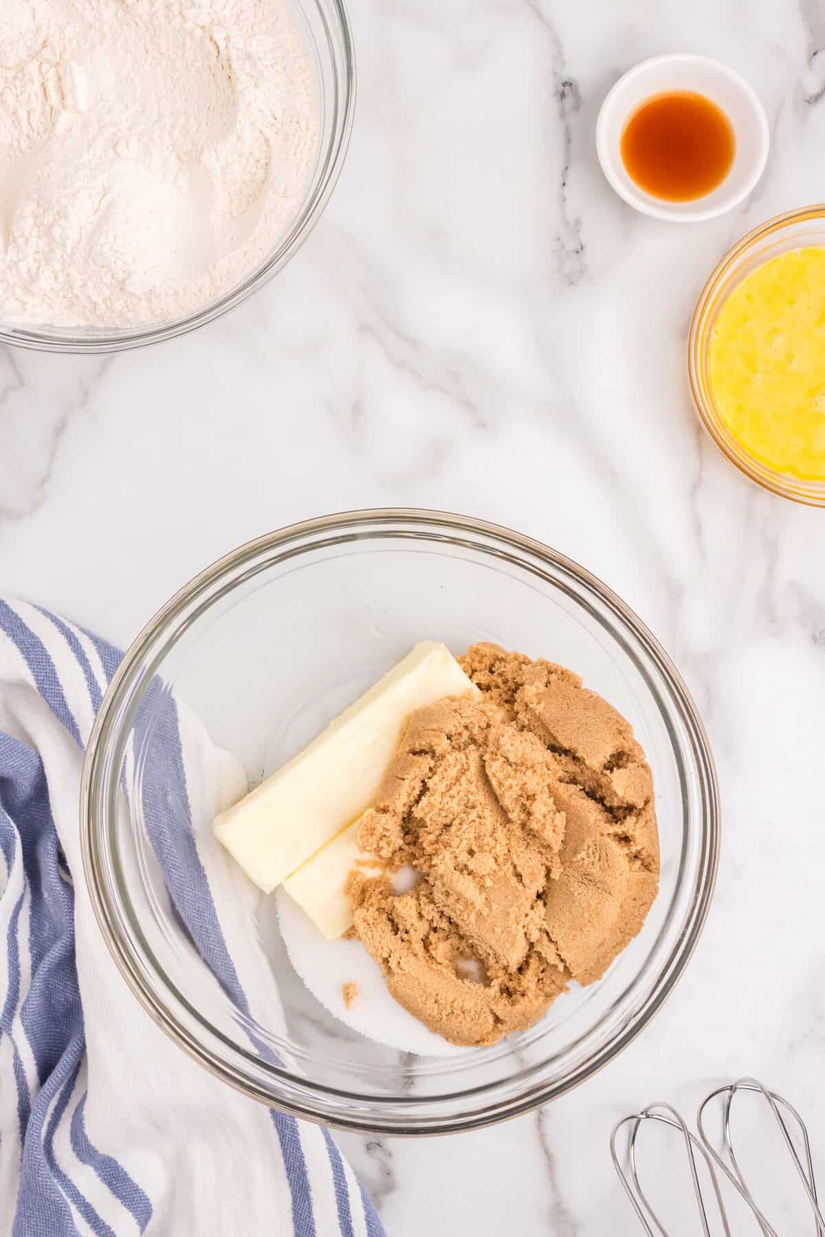 Adding brown sugar and butter to dry ingredients for White Chocolate Macadamia Nut Cookies in glass mixing bowl