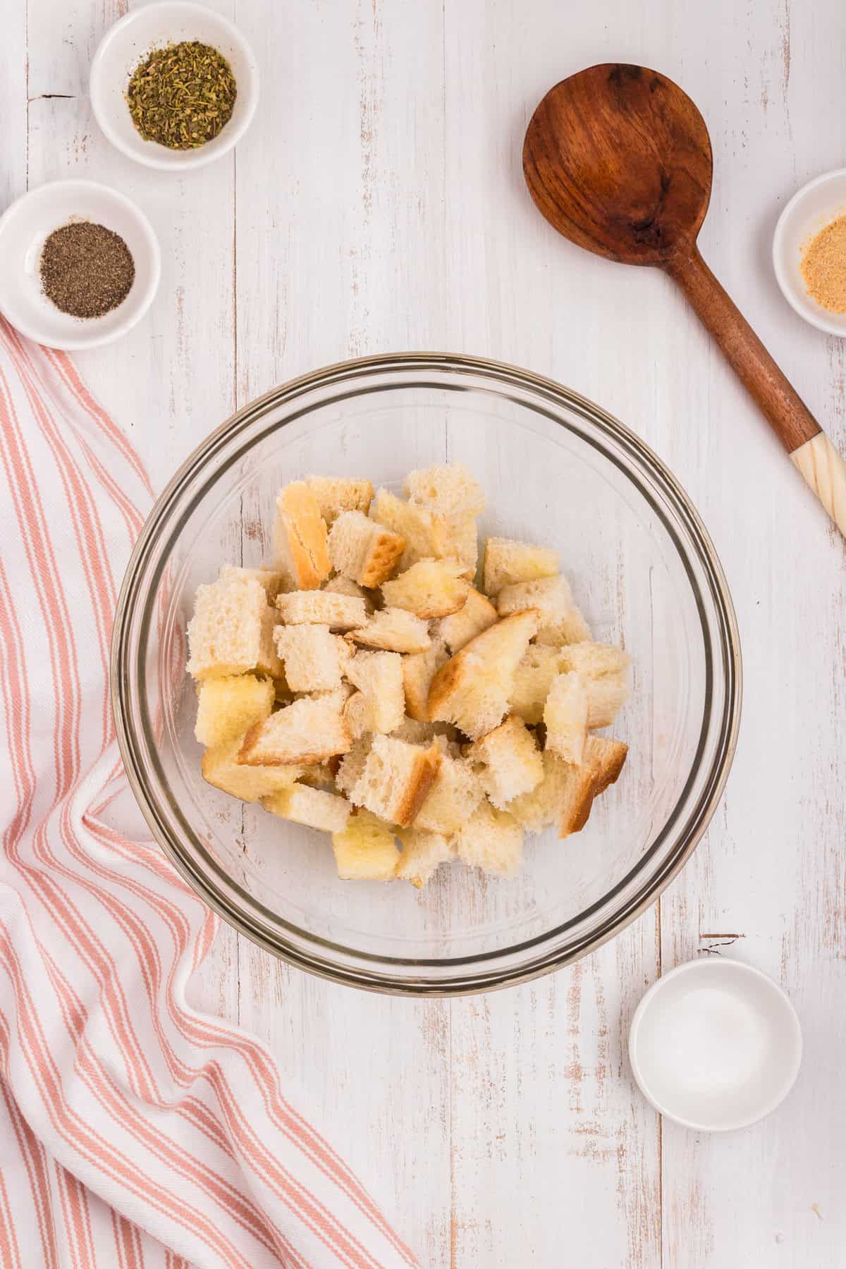 Cubed bread with melted butter over top in glass mixing bowl for Air Fryer Croutons