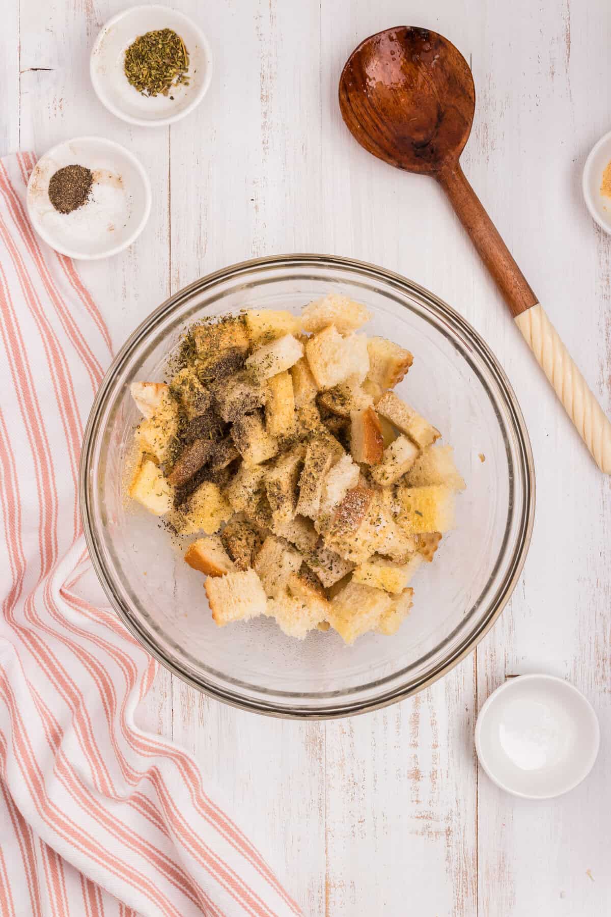 Adding seasoning over butter drenched bread cubes for Air Fryer Croutons in glass mixing bowl
