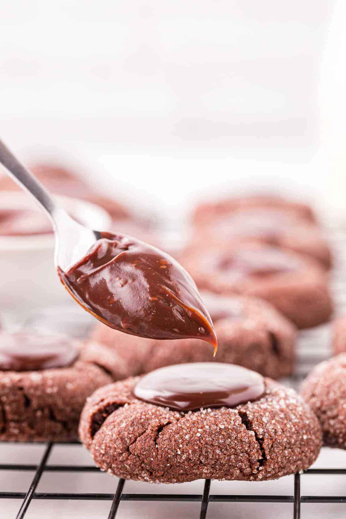 Spooning chocolate ganache into the indents of the baked cookies for Chocolate Thumbprint Cookies recipe