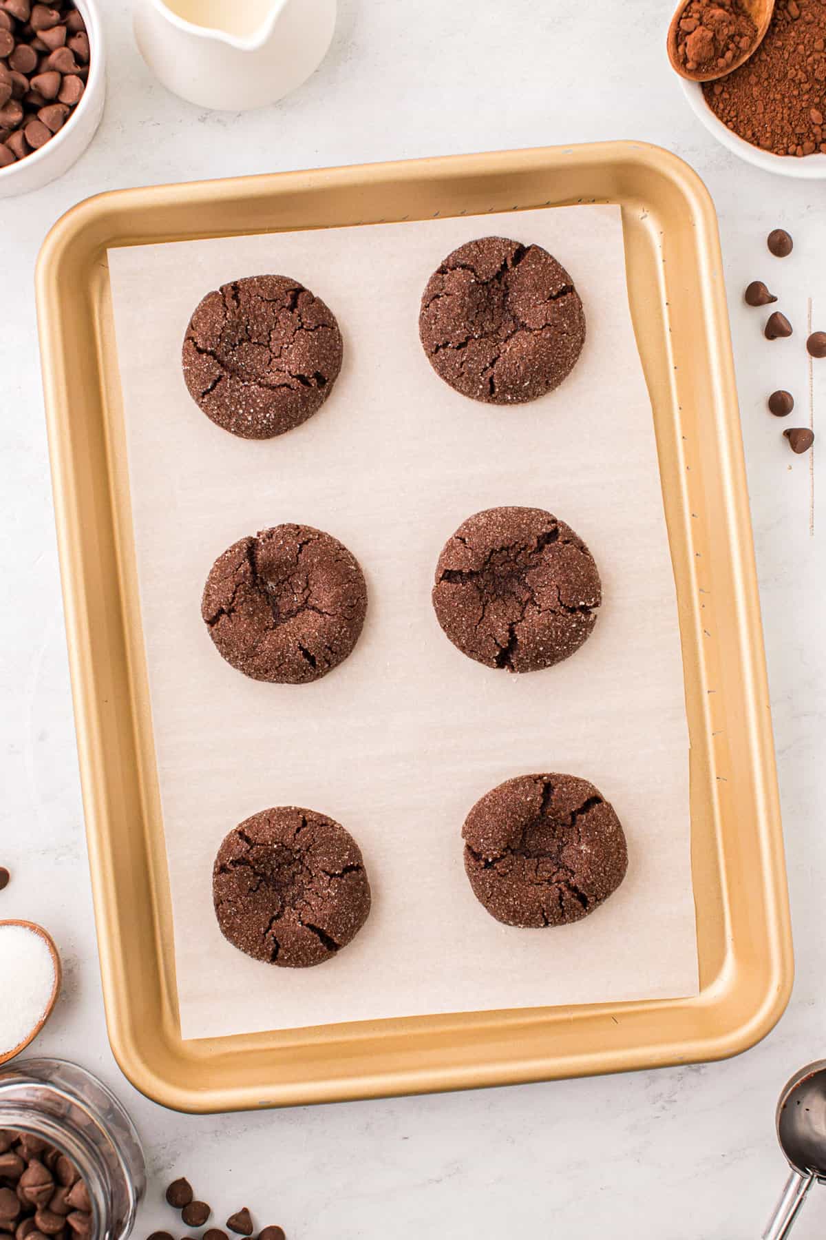 Baked Chocolate Thumbprint Cookies on parchment-lined cookie sheet hot out of the oven with an indent made with the backside of spoon