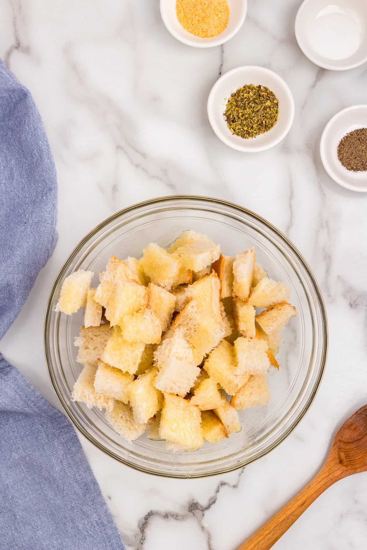 Cubed bread with melted butter over top in glass mixing bowl for Homemade Croutons