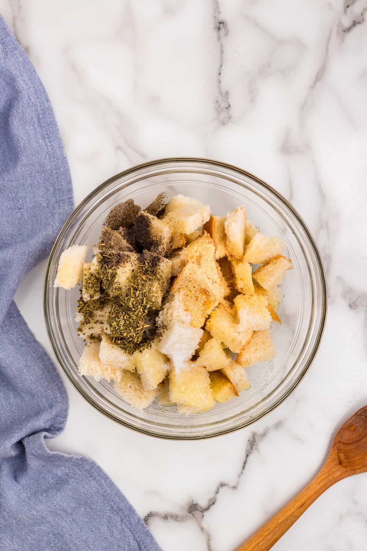 Adding seasoning over butter drenched bread cubes for Homemade Croutons in glass mixing bowl