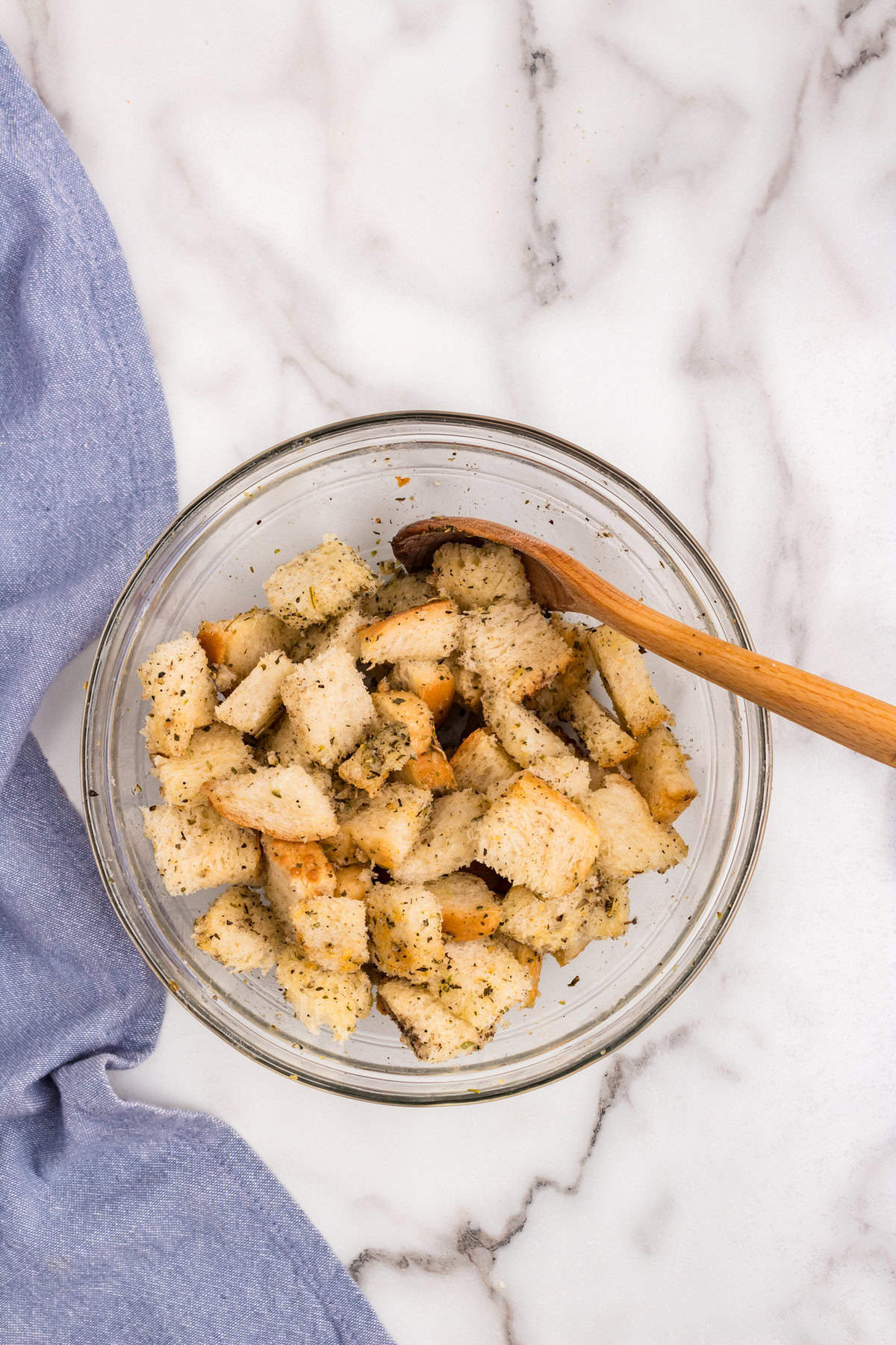 Using wooden spoon to toss coated bread cubes in glass bowl