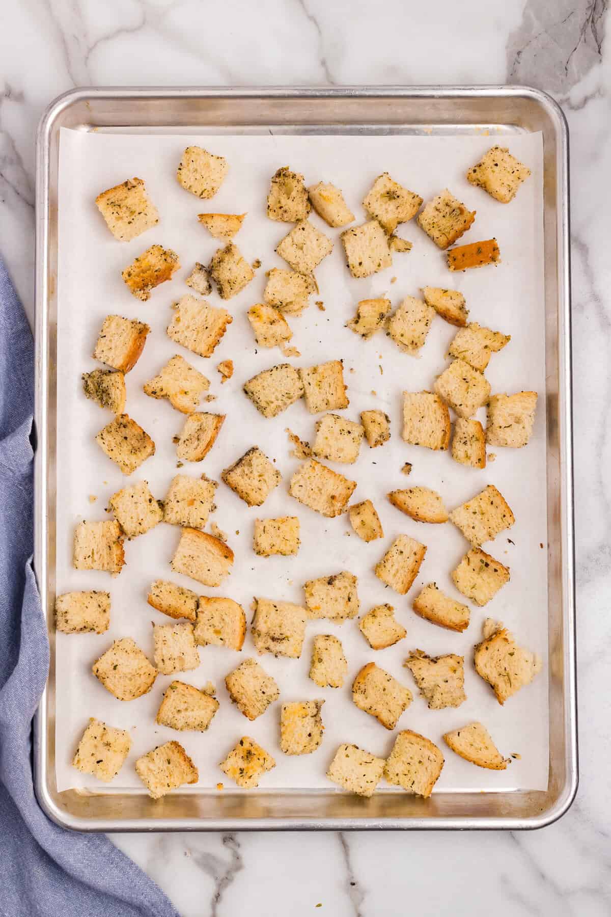 Arranging seasoned bread cubes on parchment-lined baking sheet for Homemade Croutons recipe