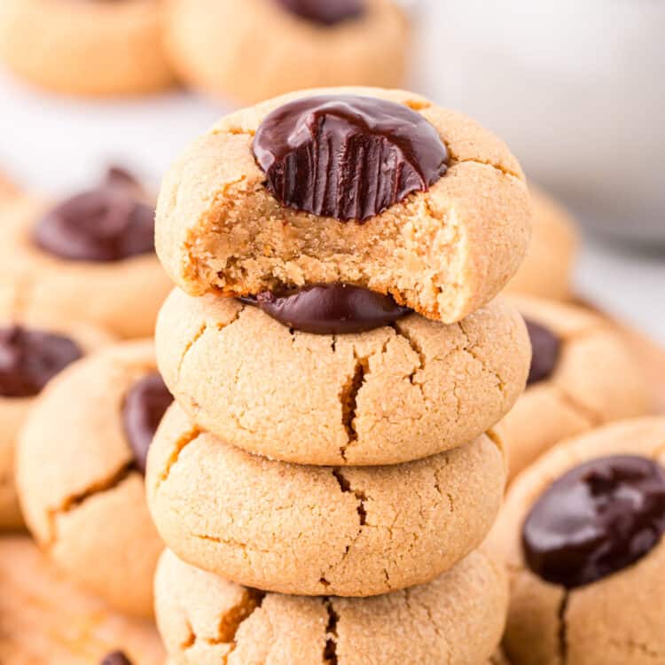 Peanut Butter Thumbprint Cookies stacked on wood cutting board with one bite taken