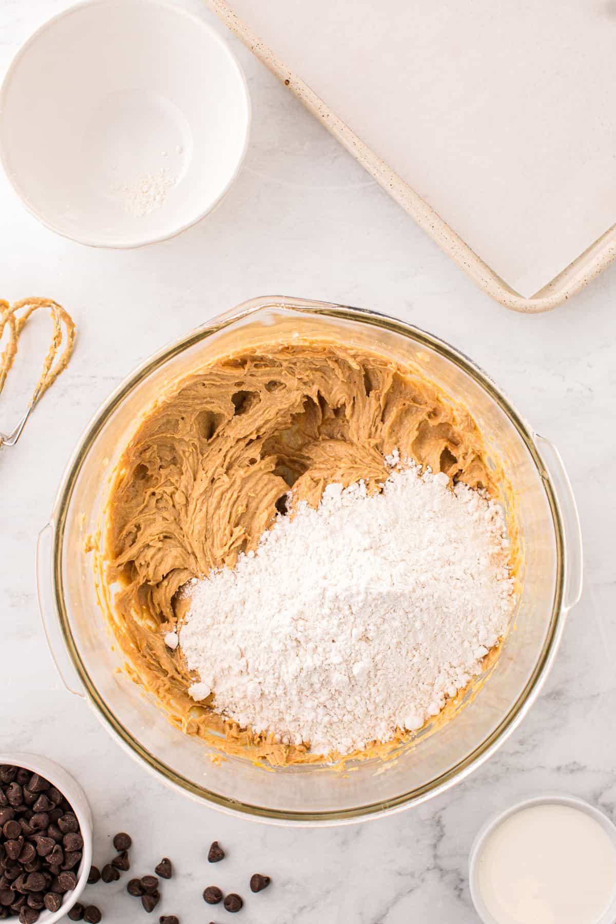 Adding flour to Peanut Butter Thumbprint Cookies dough mixture in glass bowl