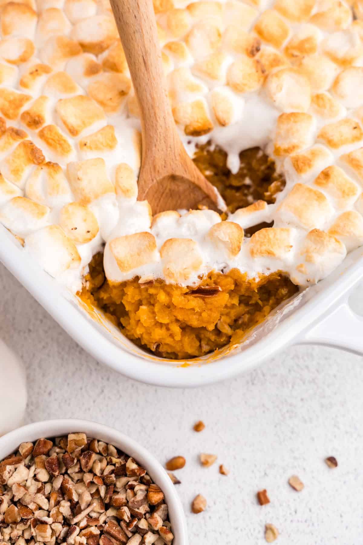 Close up picture of sweet potato casserole in a white pan with a wooden spoon scooping out casserole.
