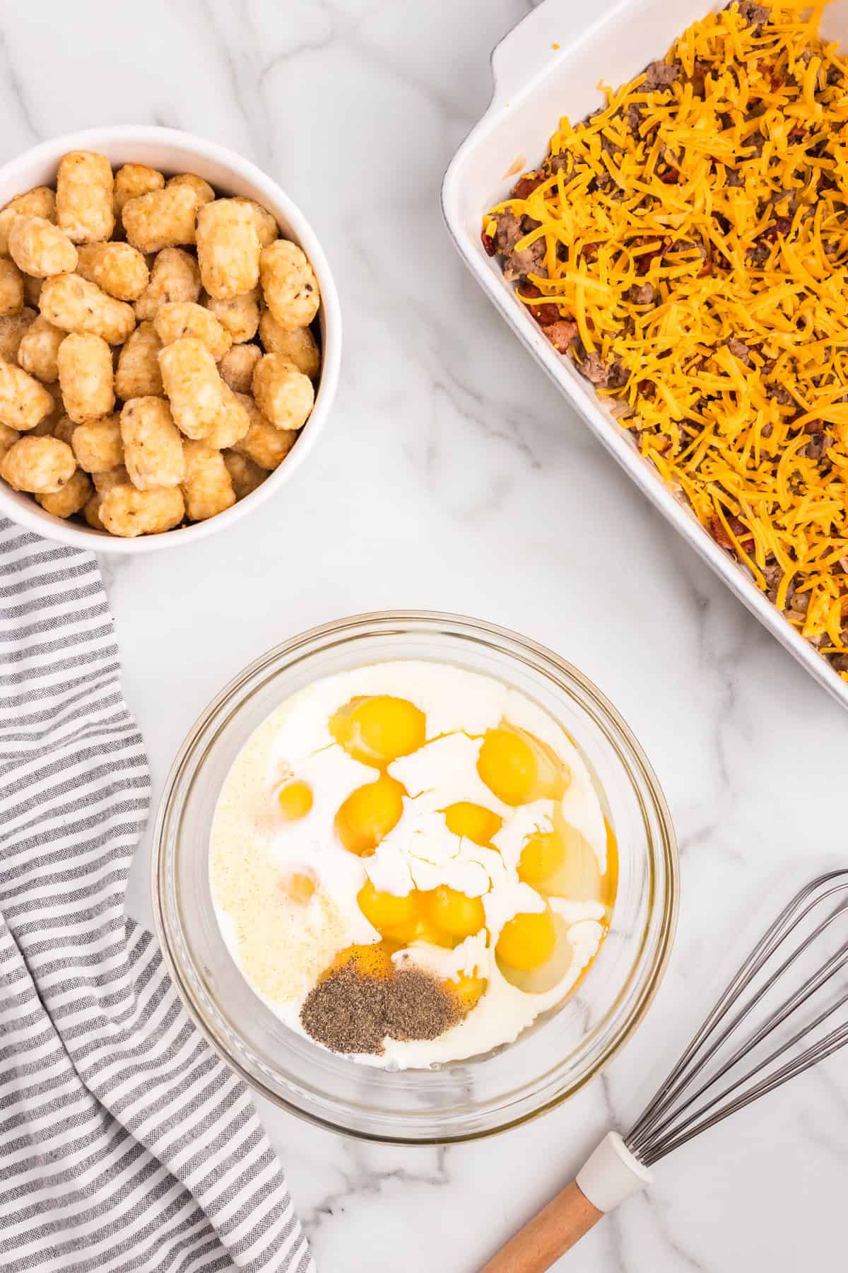 Overhead picture with tater tots and half prepped casserole in corners with egg, milk and seasonings in a glass bowl