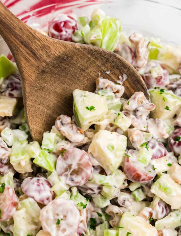 Using wooden spoon to scoop first bite of Waldorf Salad from serving bowl