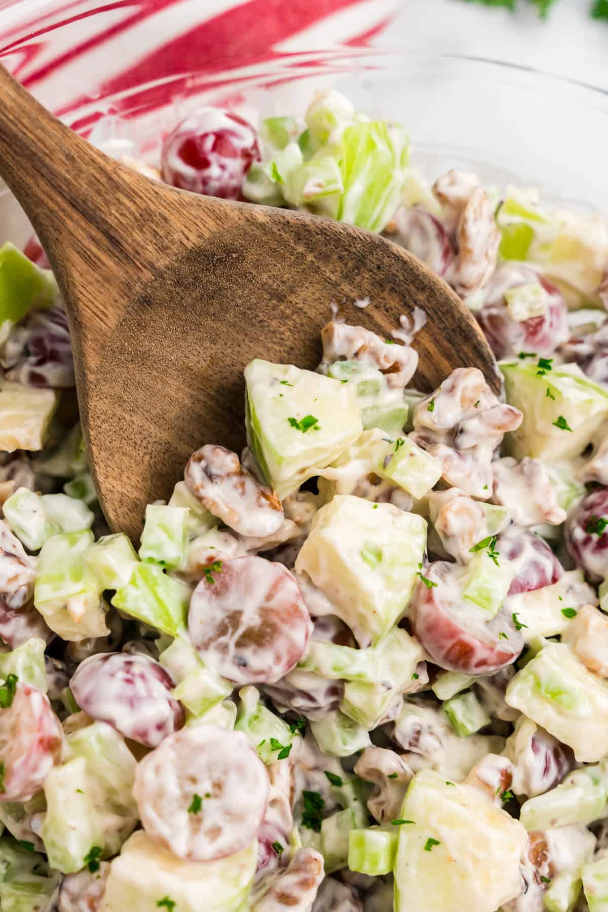 Wooden spoon scooping for bite of Waldorf Salad from serving bowl