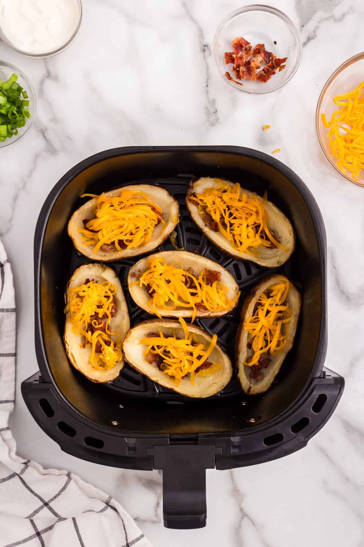 Adding cheese and bacon to potatoes in air fryer for Air Fryer Potato Skins recipe