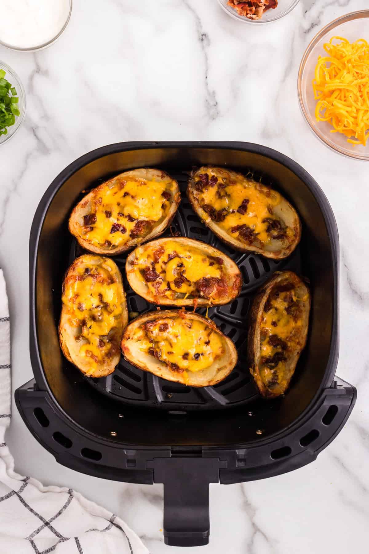 Melted shredded cheese and bacon atop potato skins in air fryer for Air Fryer Potato Skins recipe