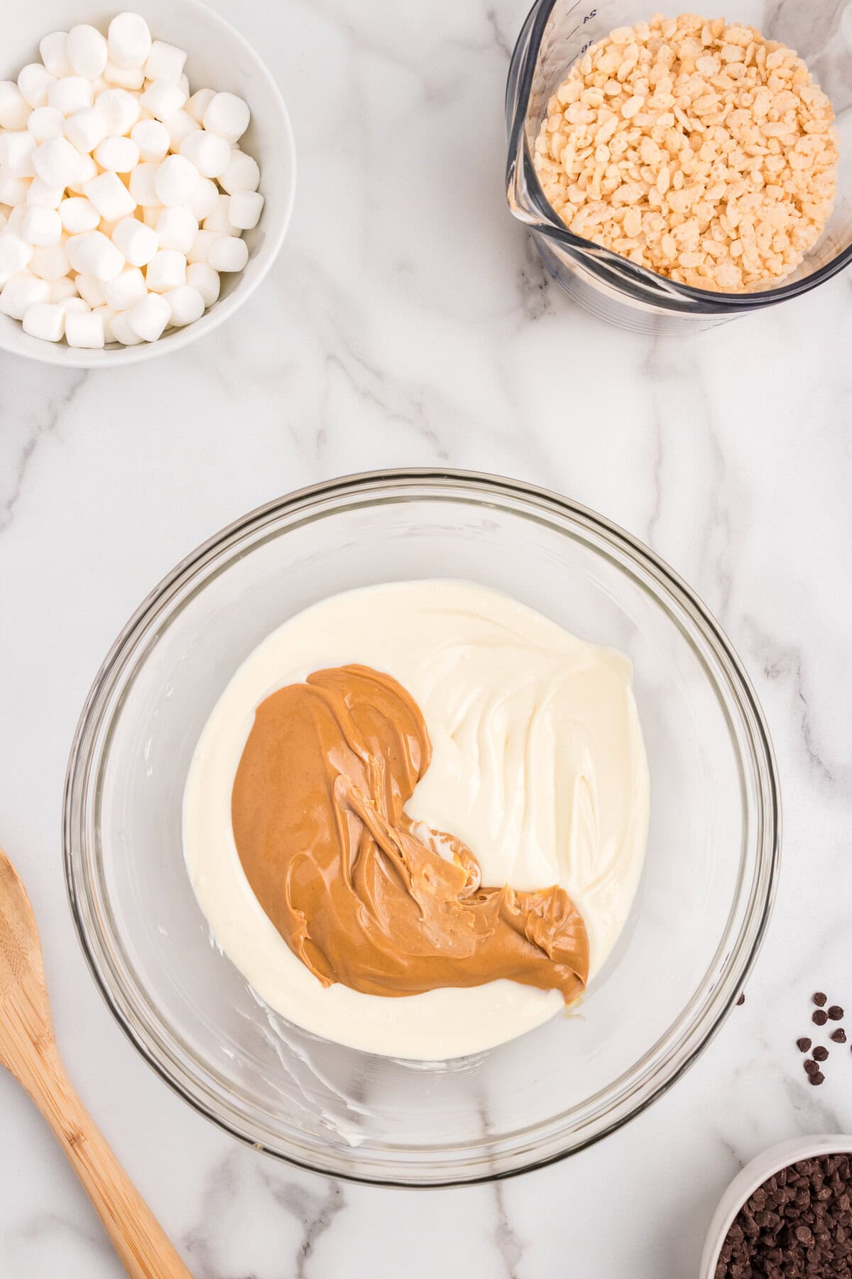 Adding creamy peanut butter to melted bark for Avalanche Cookies in glass mixing bowl