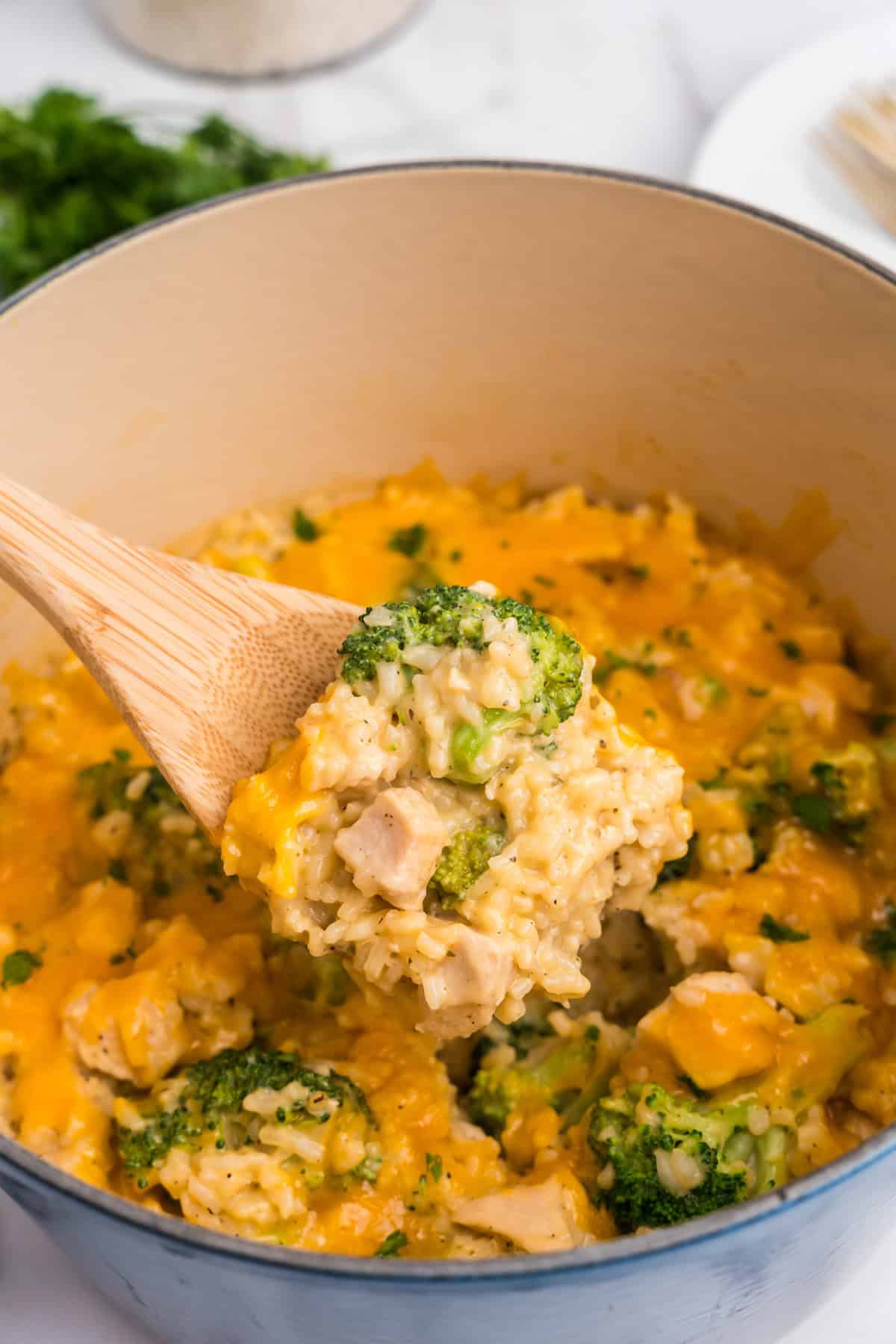 Close up picture of dutch oven with a wooden spoon scooping cheesy chicken broccoli and rice casserole.